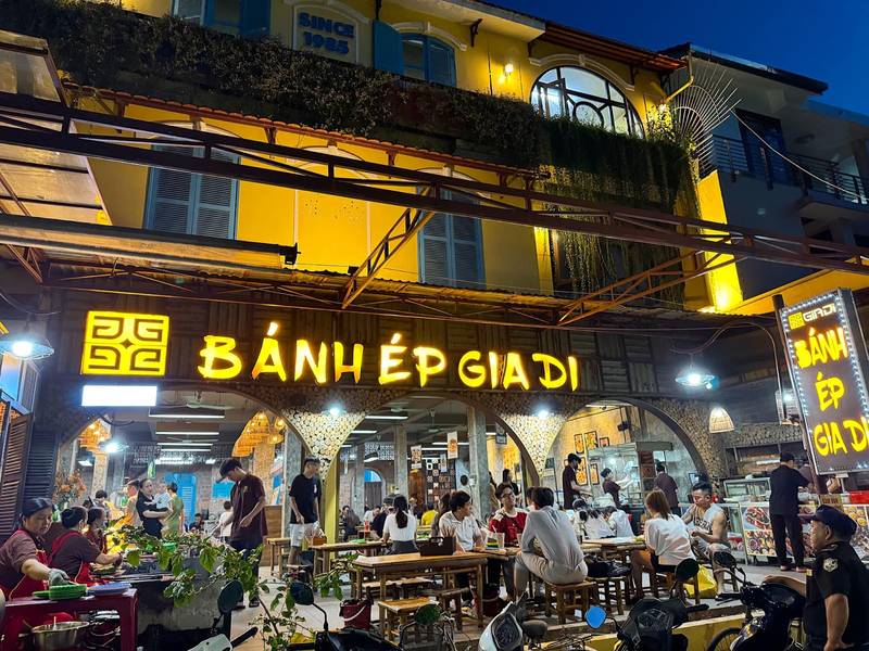 Mặt tiền Bánh Ép Gia Di sáng đèn buổi tối với khách ngồi kín